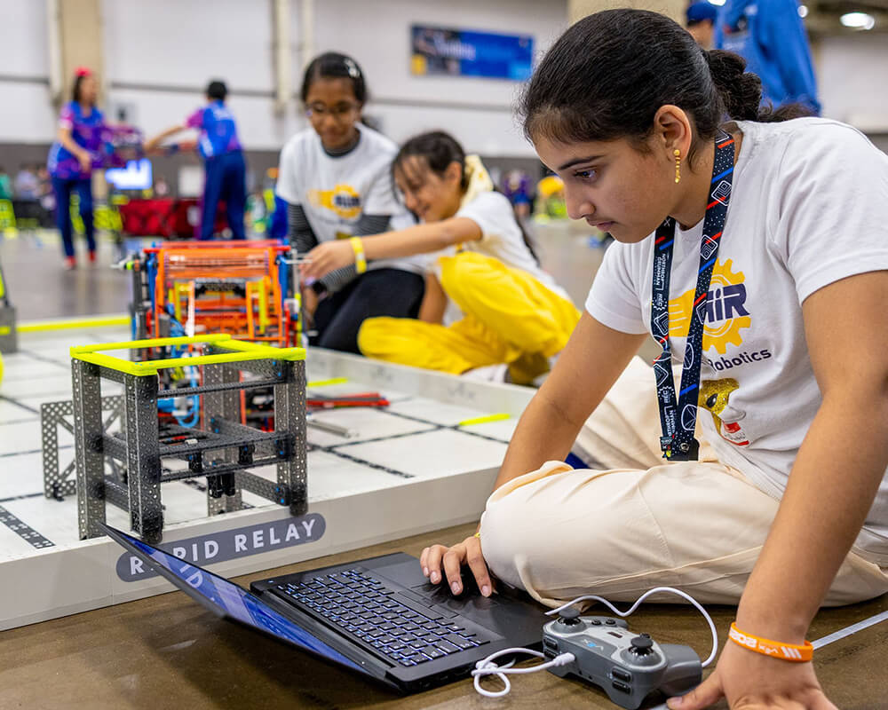 A young girl studying her code next to her robot.